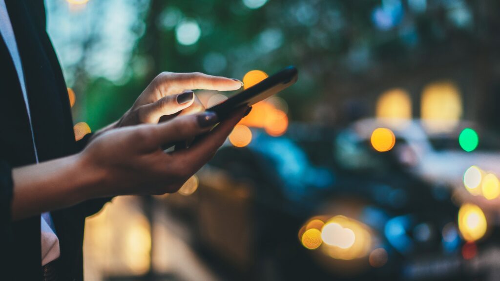 Reisende Frau ruft Handy warten gelbes Taxi in Abend Straße Europa Stadt Barcelona. Mädchen Tourist mit Smartphone Internet online Gadget Handy auf Hintergrund Bokeh Scheinwerfer von Autos